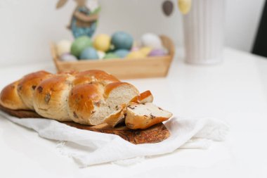 Beyaz masadaki ahşap tabakta kesilmiş paskalya ekmeği paskalya süslemeleri ile bulanık arkaplan.