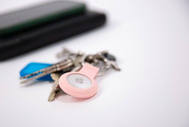 Anahtarları beyaz masada elmalı bir AirTag ile kapat, akıllı telefon ve cüzdan ile bulanık arkaplan 