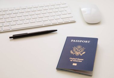 Beyaz masadaki siyah tavalı, klavyesi ve faresi olan bir Amerikan pasaportunu kapat.