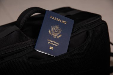 Siyah bir seyahat çantası cebinde, bulanık arka planda bir Amerikan pasaportunu kapat.