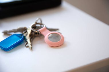 Anahtarları beyaz masada elmalı bir AirTag ile kapat, akıllı telefon ve cüzdan ile bulanık arkaplan 