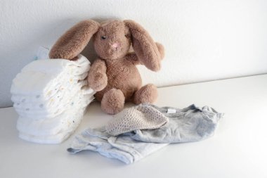 Bir yığın bebek bezi, tulumlar ve beyaz soyunma masasında pelüş bir tavşan. 