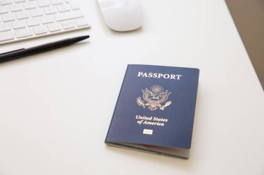 Beyaz masadaki siyah tavalı, klavyesi ve faresi olan bir Amerikan pasaportunu kapat.