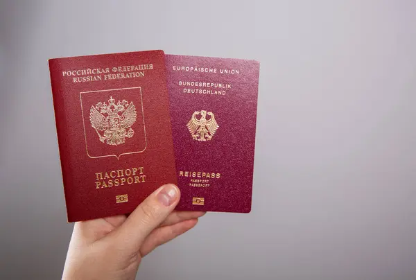 stock image Close up of a female hand holding a German and a Russian passport, empty copy space background