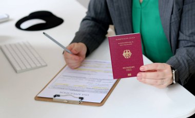 Beyaz bir kadının ofis masasında Alman pasaportu ile vize başvuru formlarını doldurmasının üst görüntüsü.