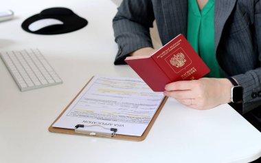 Beyaz bir kadının ofis masasında Rus pasaportu ile vize başvurusu formu doldurmasının üst görüntüsü.