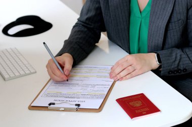 Beyaz bir kadının ofis masasında Rus pasaportu ile vize başvurusu formu doldurmasının üst görüntüsü.