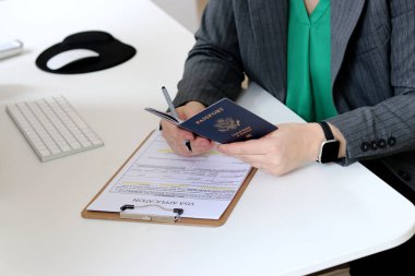 Beyaz bir kadının ofis masasında Amerikan pasaportu ile vize başvuru formlarını doldurmasının üst görüntüsü.
