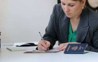 Kafkasyalı bir kadının vize başvuru formlarını doldururken ofis masasında Amerikan pasaportu, vize belgesi konsepti...