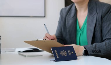 Kafkasyalı bir kadının elinde vize başvuru kâğıdı belgesi ve ofis masasında yatan Amerikan pasaportu, vize belgesi konsepti.