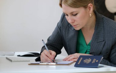 Kafkasyalı bir kadının vize başvuru formlarını doldururken ofis masasında Amerikan pasaportu, vize belgesi konsepti...