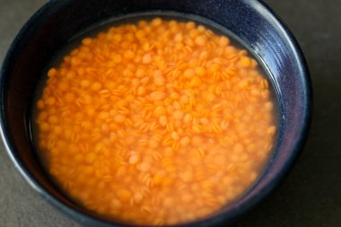 Sağlıklı yemek tarifleri için gri mutfak masasında mavi bir kaseye batırılmış kırmızı mercimekleri kapatın. 