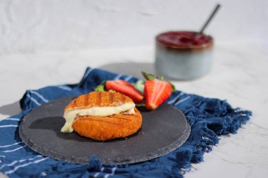 Kase içinde çilek soslu taze peynirli kızarmış camembert peyniri, gri taş tabak ve mavi peçete. 