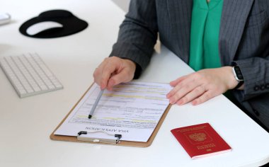 Beyaz bir kadının ofis masasında Rus pasaportu ile vize başvurusu formu doldurmasının üst görüntüsü.