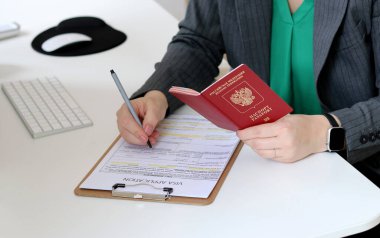 Beyaz bir kadının ofis masasında Rus pasaportu ile vize başvurusu formu doldurmasının üst görüntüsü.