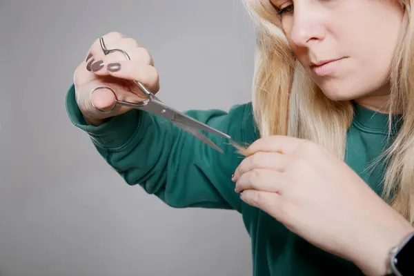 stock image Close up portrait of a blonde Caucasian woman in a green sweater cutting her own hair at home, grey empty background