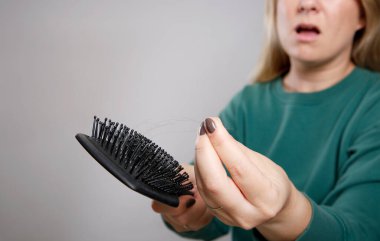 Mutsuz sarışın bir kadının saçını siyah bir saç fırçasında bulmasına yakından bakın. Saç dökülmesi konsepti. Gri arkaplan duvarı