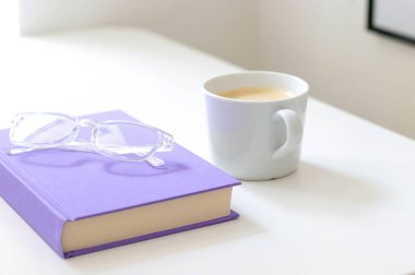 Mor renkli, şeffaf bardaklar ve beyaz masanın üzerinde beyaz bir fincan kahve olan bir kitap. Metin için ücretsiz kopyalama alanı. Eğitim ve okuma kitabı kavramı 