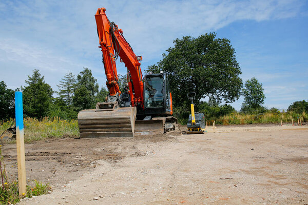 Большой оранжевый экскаватор, стоящий на месте строительства. Построение концепции семейного дома