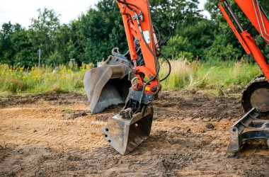 İnşaat alanının zemininde duran turuncu bir kazıcı. Aile evi konsepti inşa etmek