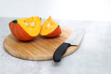 Ahşap bir tahtanın üzerinde kesilmiş taze bir Hokkaido kabağı ve arka planda gri bir masa. 