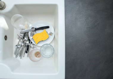 Beyaz seramik mutfak lavabosu kirli bulaşıklarla dolu, koyu gri masa.