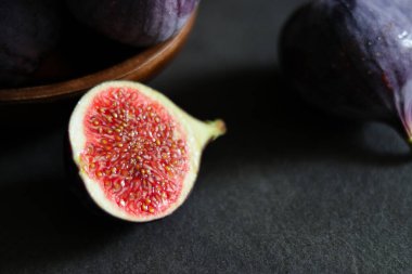 Koyu gri masadaki ahşap bir kasede olgun incir meyvelerini yakın..