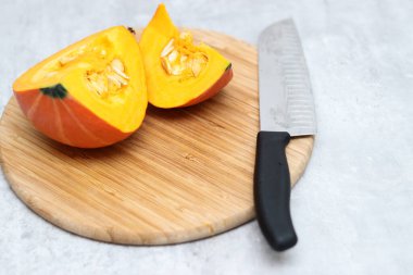 Ahşap bir tahtanın üzerinde kesilmiş taze bir Hokkaido kabağı ve arka planda gri bir masa. 