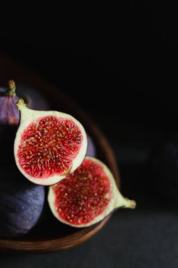 Koyu gri masadaki ahşap bir kasede olgun incir meyvelerini yakın..