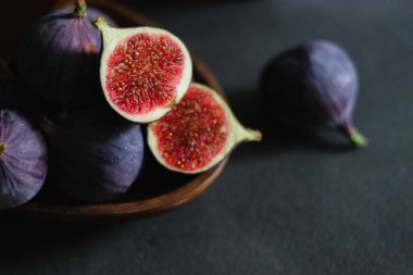 Koyu gri masadaki ahşap bir kasede olgun incir meyvelerini yakın..