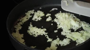 Siyah bir tavada kızartılmış çiğ soğan, soğan ve yağ spreyli gri mutfak masası.
