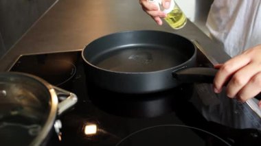 Bir kadının siyah bir tavada şişeden yemek yağını gözetlediği yakın plan. Sağlıklı beslenme ve daha az kalori diyeti 
