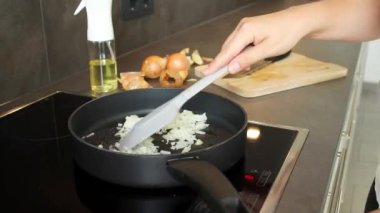 Siyah bir tavada çiğ soğan karıştıran bir kadın elini kapayın. Spatula, soğan ve yağ spreyiyle bulanık bir arkaplan.