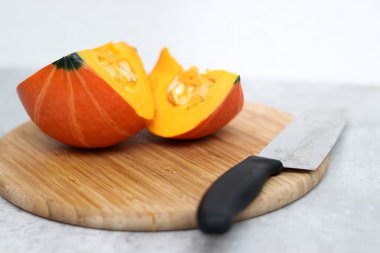 Ahşap bir tahtanın üzerinde kesilmiş taze bir Hokkaido kabağı ve arka planda gri bir masa. 