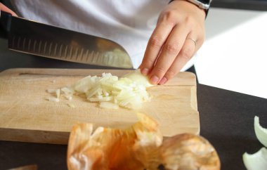 Kadın ellerinin ahşap tahtada çiğ beyaz soğan kesmesi, bulanık arka plan.