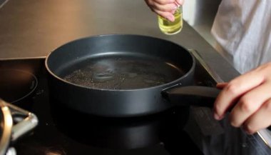 Bir kadının siyah bir tavada şişeden yemek yağını gözetlediği yakın plan. Sağlıklı beslenme ve daha az kalori diyeti 