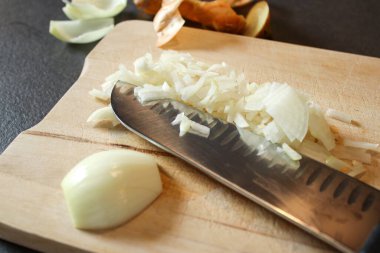 Tahta bir tahtanın üzerinde kesilmiş beyaz soğanı bıçakla kapat, koyu gri mutfak masası. 