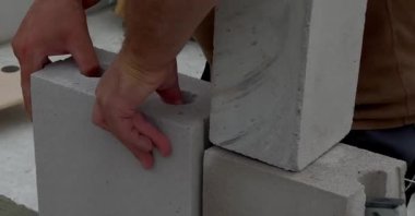 Duvarda beyaz taş ve beton yapıştırıcıyla duvar döşeyen bir inşaat işçisinin yakınına. Ev inşa etme kavramı 