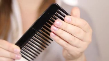 Sarışın bir kadının saçını tarağın üzerinde bulmasını yakından çek. Saç dökülmesi konsepti. Beyaz bulanık arka plan duvarı. Yüksek kaliteli FullHD görüntüler