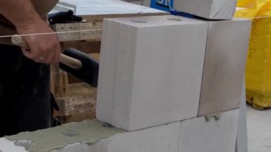 Duvarda beyaz taş ve beton yapıştırıcıyla duvar döşeyen bir inşaat işçisinin yakınına. Ev inşa etme kavramı 