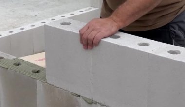 Duvarda beyaz taş ve beton yapıştırıcıyla duvar döşeyen bir inşaat işçisinin yakınına. Ev inşa etme kavramı 