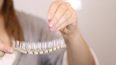 Sarışın bir kadının saçını bir saç fırçasında bulmasına yakın çekim. Saç dökülmesi konsepti. Beyaz banyo arka plan duvarı. Yüksek kaliteli FullHD görüntüler