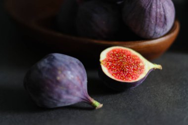 Koyu gri masadaki ahşap bir kasede olgun incir meyvelerini yakın..