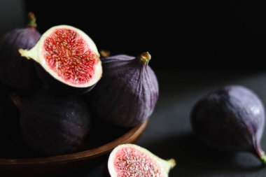 Koyu gri masadaki ahşap bir kasede olgun incir meyvelerini yakın..