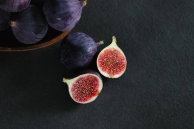 Koyu gri masadaki ahşap bir kasede olgun incir meyvelerini yakın..