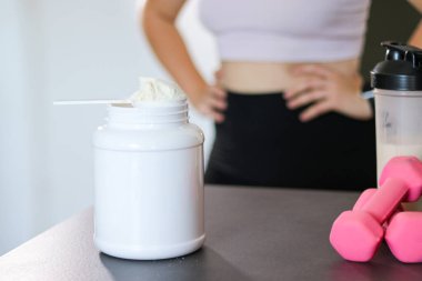 Mutfakta protein içeceği hazırlayan kadına yakın çekim. Kilo vermenin yerine diyet yemeği. Masada beyaz beyaz protein tozu ve pembe dambıllar var. 
