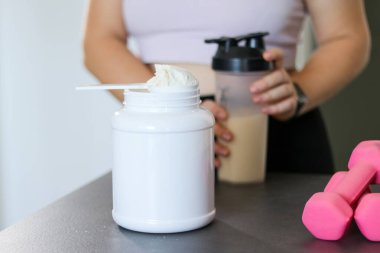 Mutfakta protein içeceği hazırlayan kadına yakın çekim. Kilo vermenin yerine diyet yemeği. Masada beyaz beyaz protein tozu ve pembe dambıllar var. 
