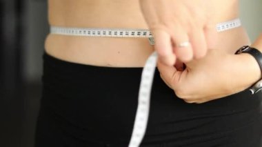 Karnını bant ile ölçen bir kadının yakın çekimi. Şişman, göbekli tiplerden. Sağlıksız yaşam tarzı diyet konsepti. Yüksek kaliteli FullHD görüntüler