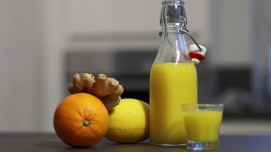 Ev yapımı portakal, limon ve zencefilli içecek. Mutfak masasında küçük bardakta, arka planda bulanık. Soğuk baca ve bağışıklık güçlendirici konsept. Yüksek kaliteli FullHD görüntüler
