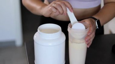 Mutfakta protein içeceği hazırlayan kadına yakın çekim. Kilo vermenin yerine diyet yemeği. Masada beyaz beyaz protein tozu ve pembe dambıllar var. 